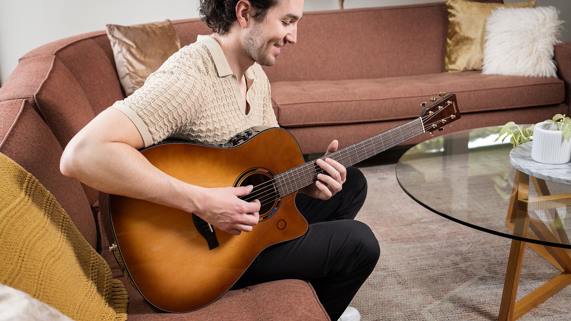 En mann som sitter i en sofa i stuen og spiller på en TAG3 C akustisk gitar