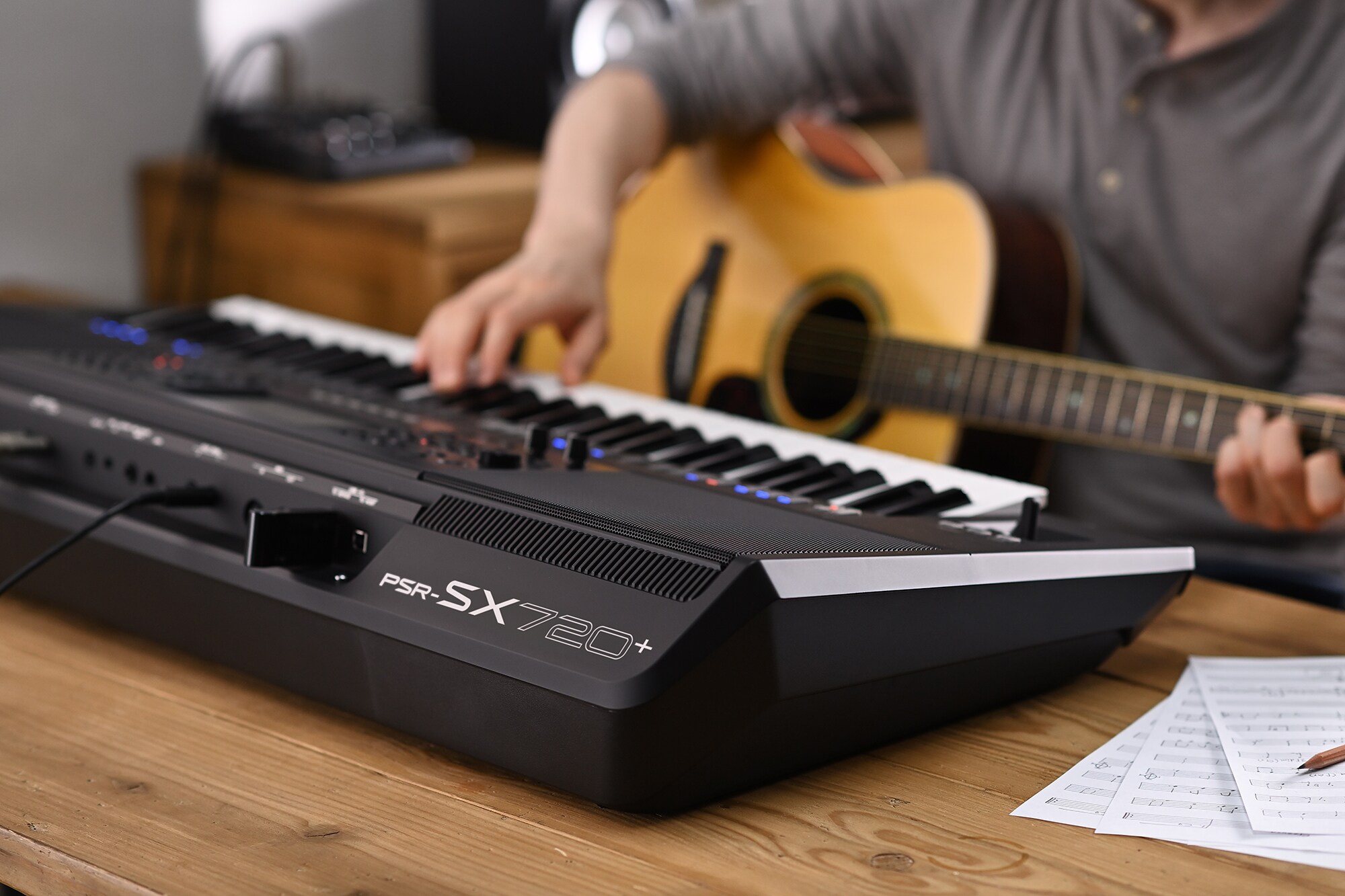 Bilde av en person som spiller på Yamaha Arranger Workstation PSR-SX720+ mens vedkommende holder en gitar
