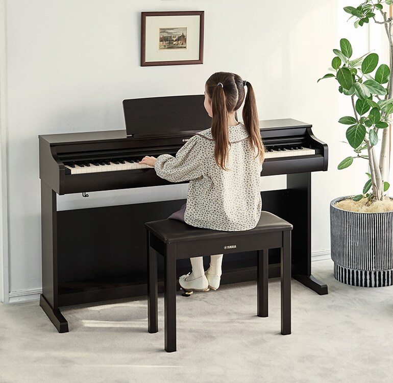 En ung jente som øver på et ARIUS-piano i en stue