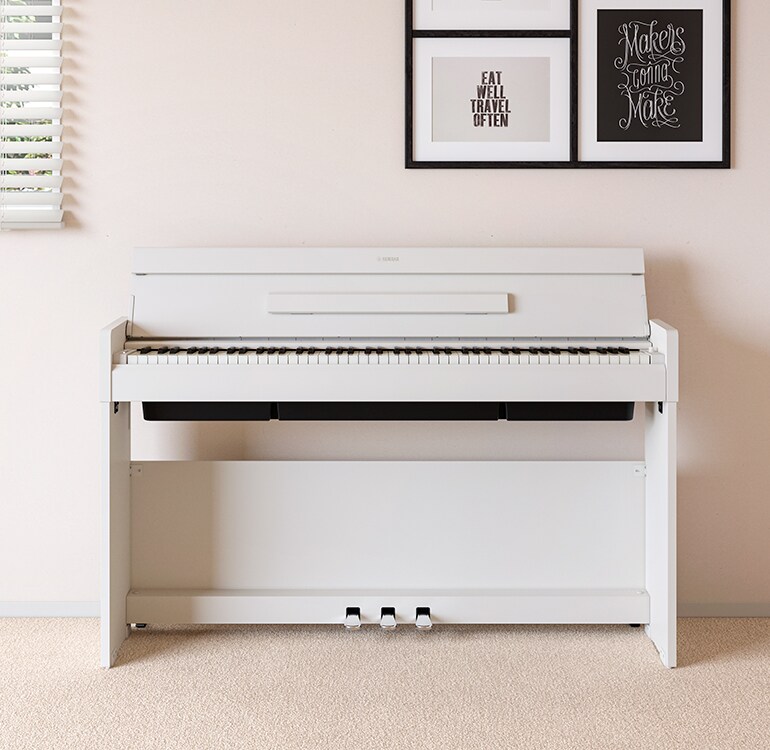 En stue med et hvitt ARIUS-piano plassert ved siden av vegghyller med lamper og en diffusor, harmonisk integrert i interiøret.