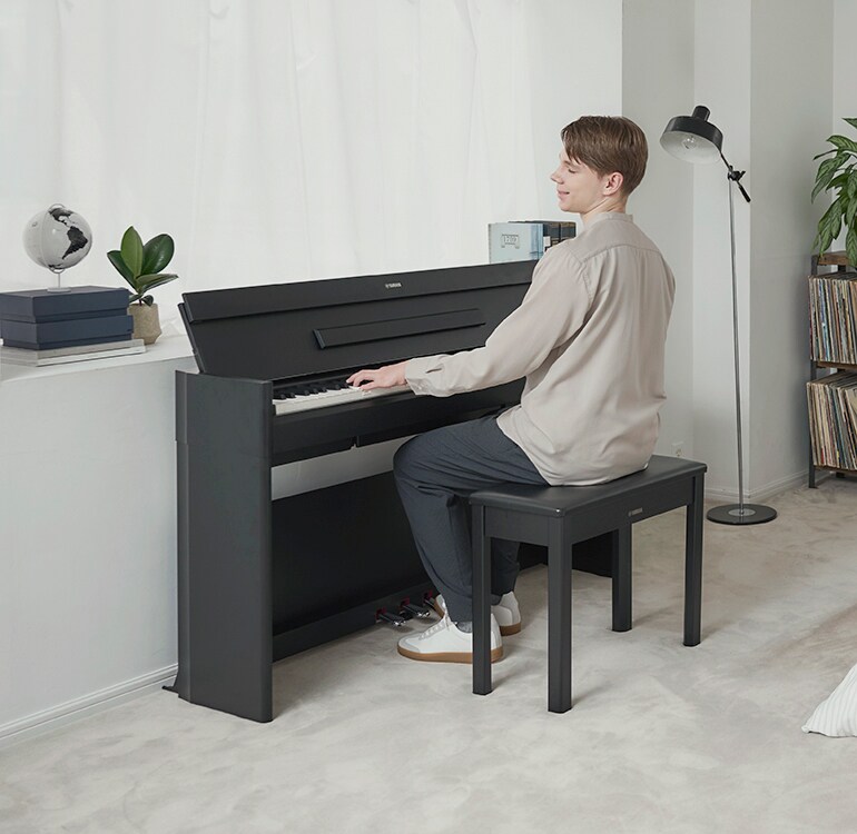 En mann som spiller på et ARIUS-piano på et soverom i avslappende omgivelser
