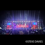 Wide view of The Experience 2025 in Lagos, Nigeria, showing a large outdoor stage with lighting and video screens performing before a crowd of worshippers during the annual gospel music event.